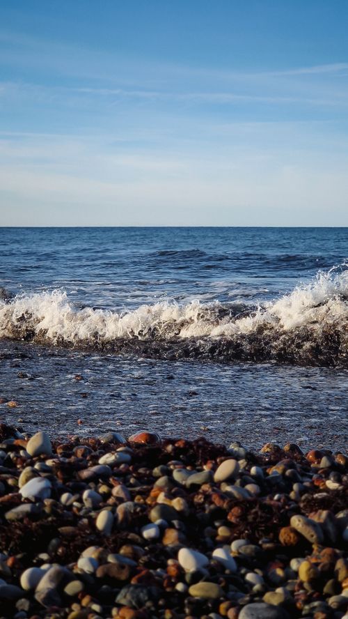 Free Stunning view of ocean waves crashing onto a rocky beach under a clear sky. Stock Photo