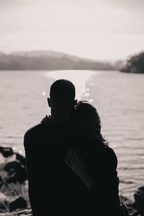 Free A couple embraces by the lake during sunset, creating a romantic silhouette. Stock Photo