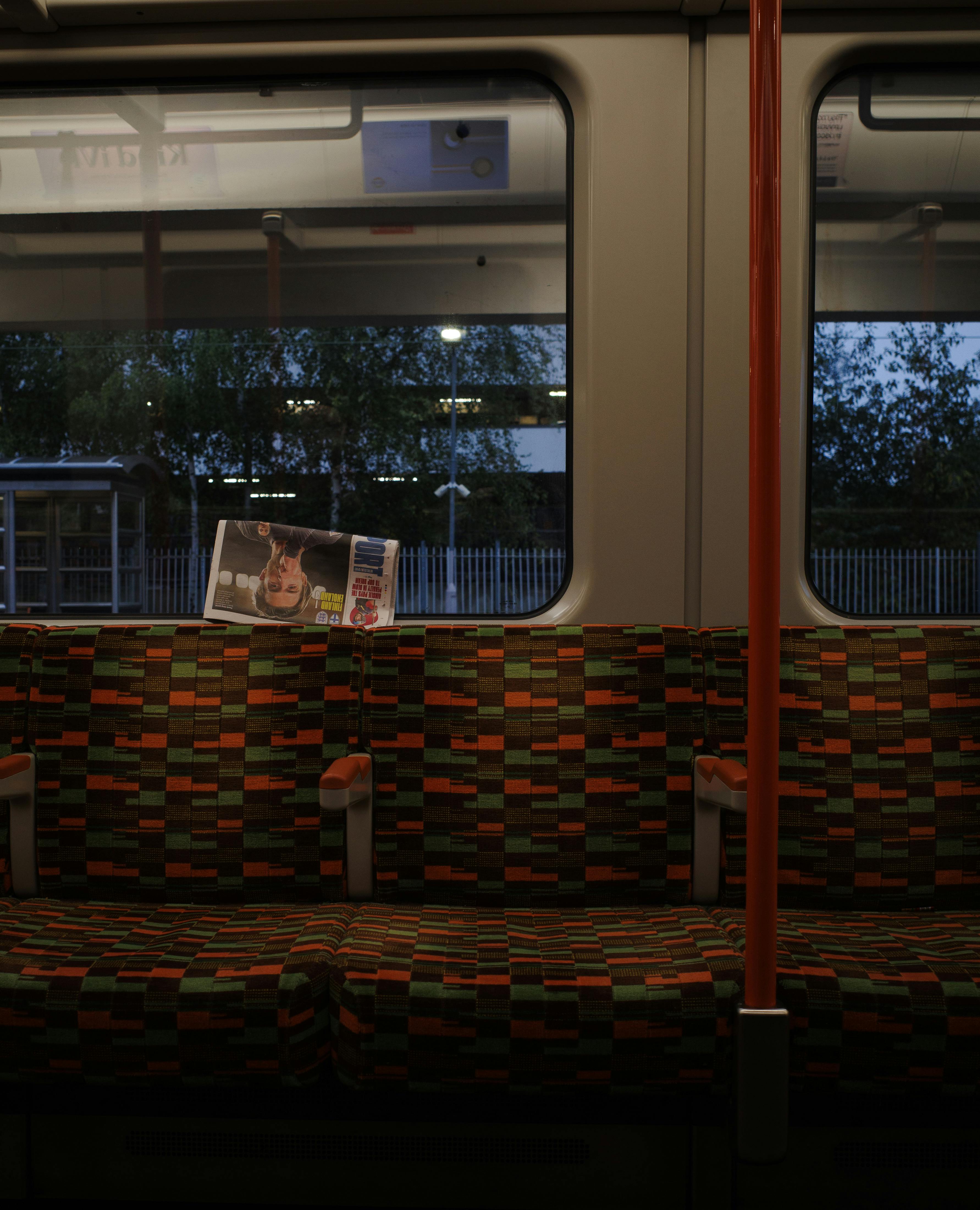 An empty train carriage with patterned seats and a newspaper, captured during nighttime.