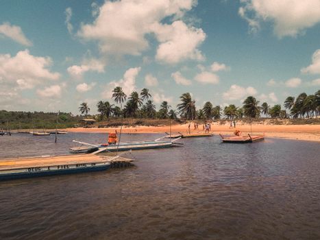 A tranquil beach scene at Barra do Cunhaú, Brazil featuring boats and palm trees under a sunny sky.