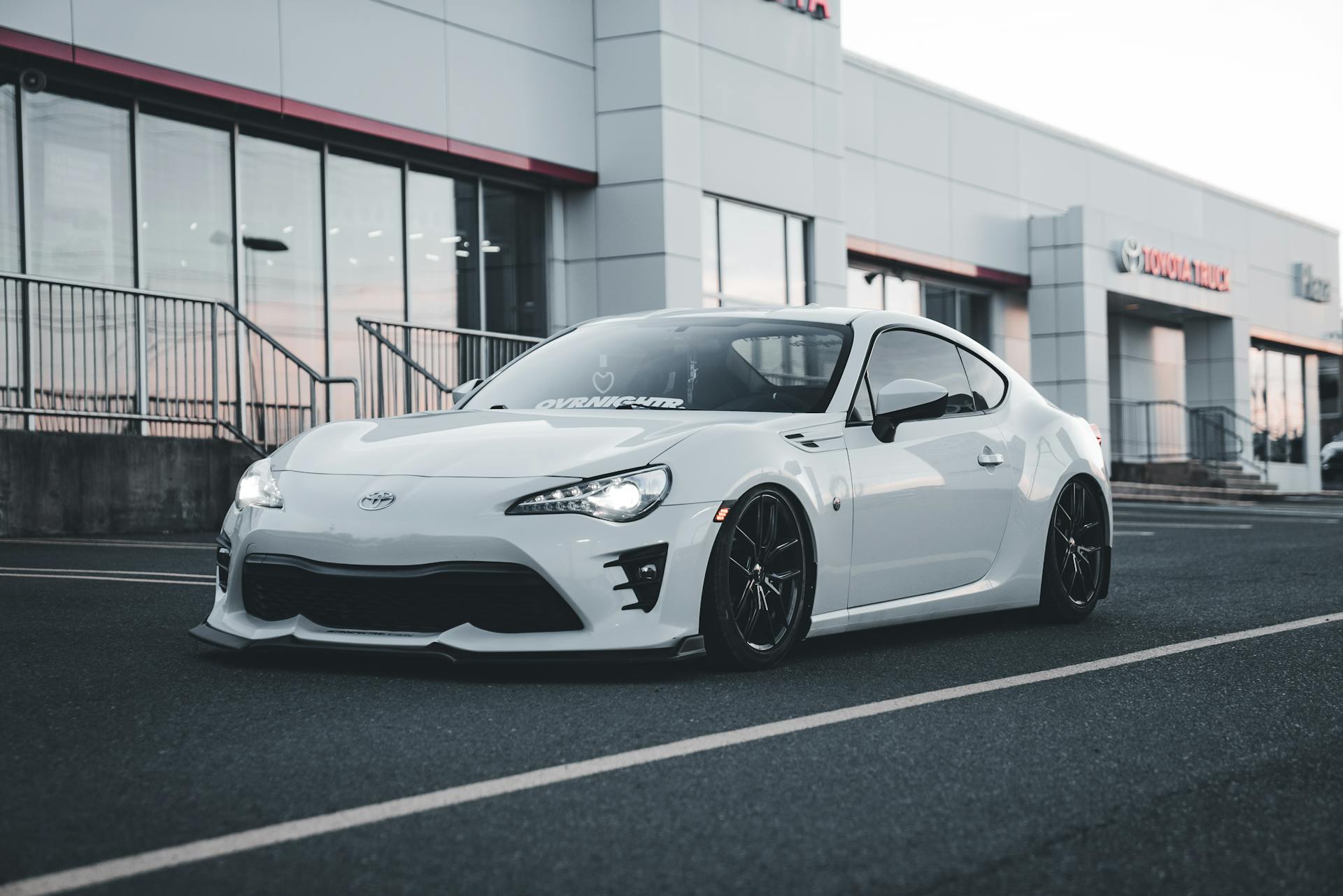 Stylish white sports car parked in front of Toyota dealership building at twilight.