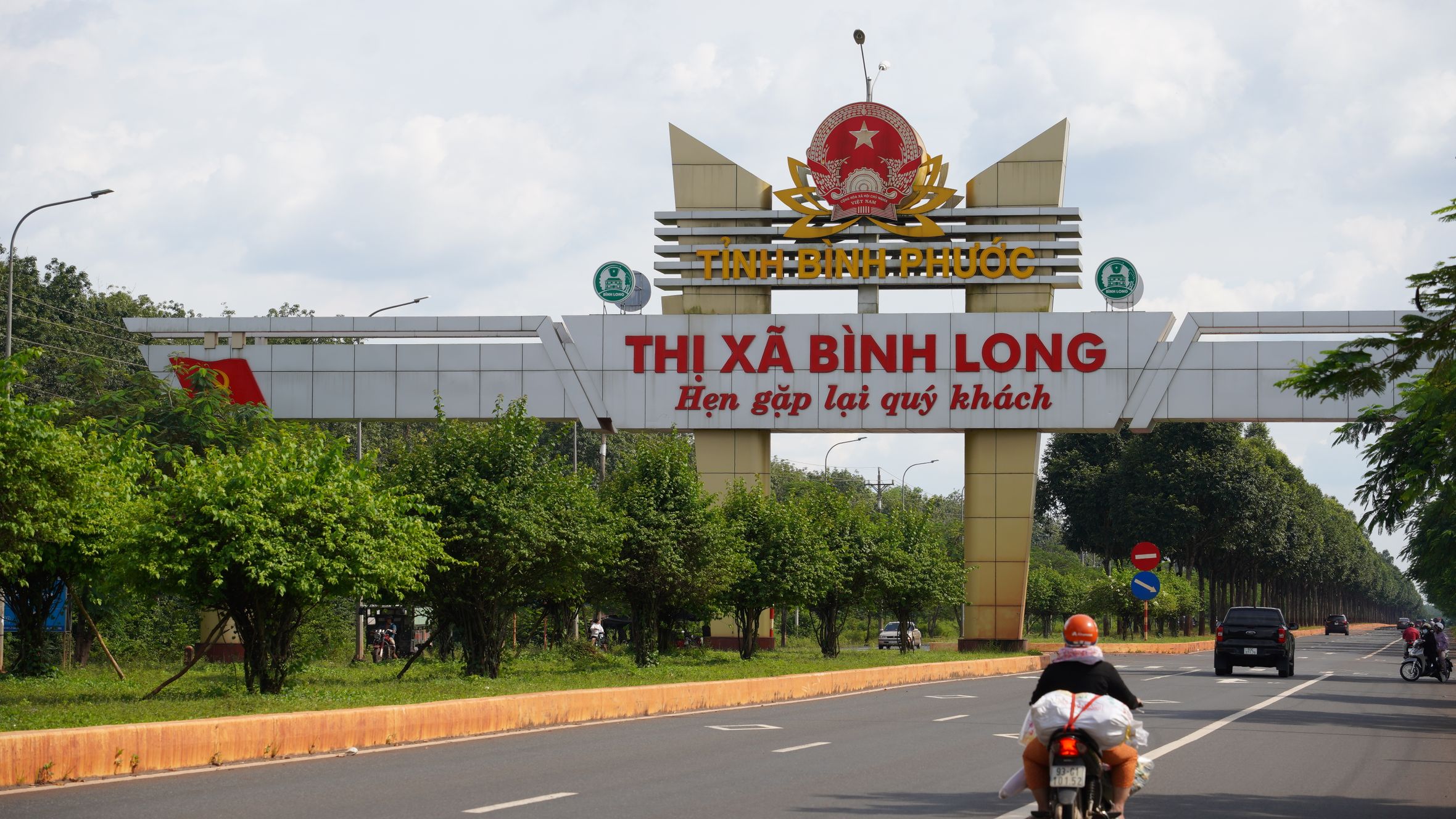 Motorcyclist travels towards the Binh Long gate in Bình Phước, Vietnam on a sunny day.