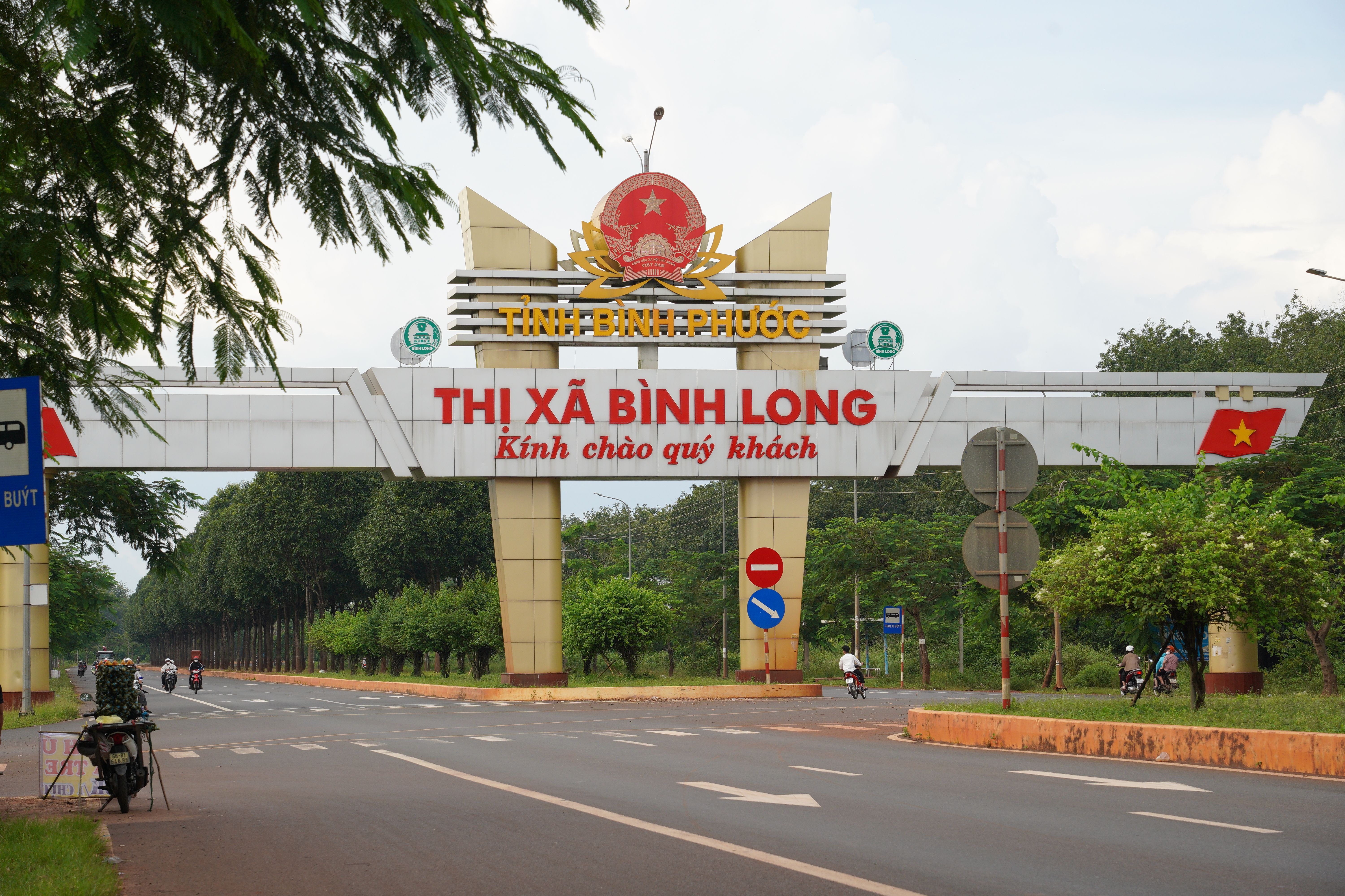View of the entrance archway to Bình Long in Bình Phước Province, Vietnam with motorbikes passing by.