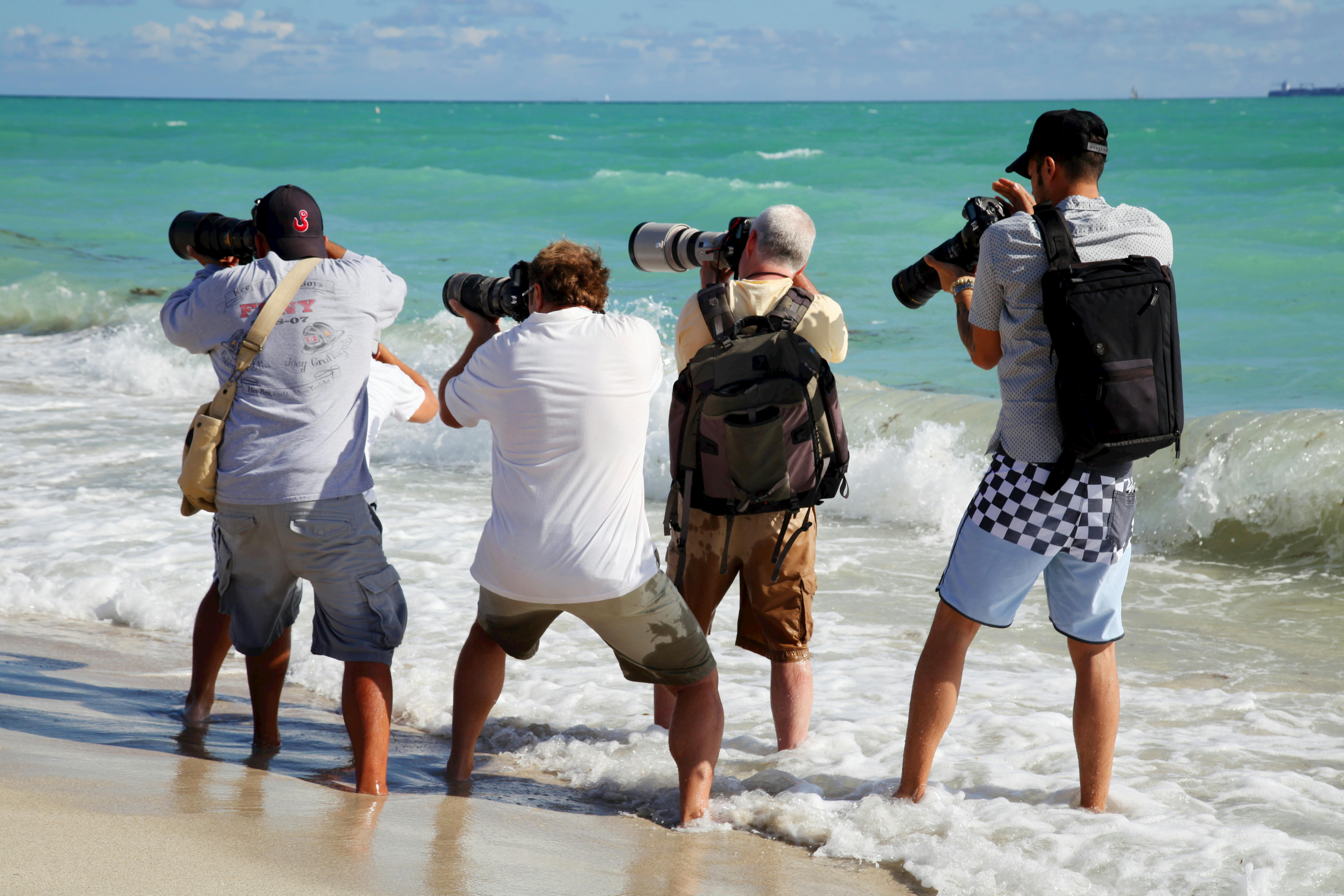 Group of male photographers taking pictures by the ocean in Miami Beach.