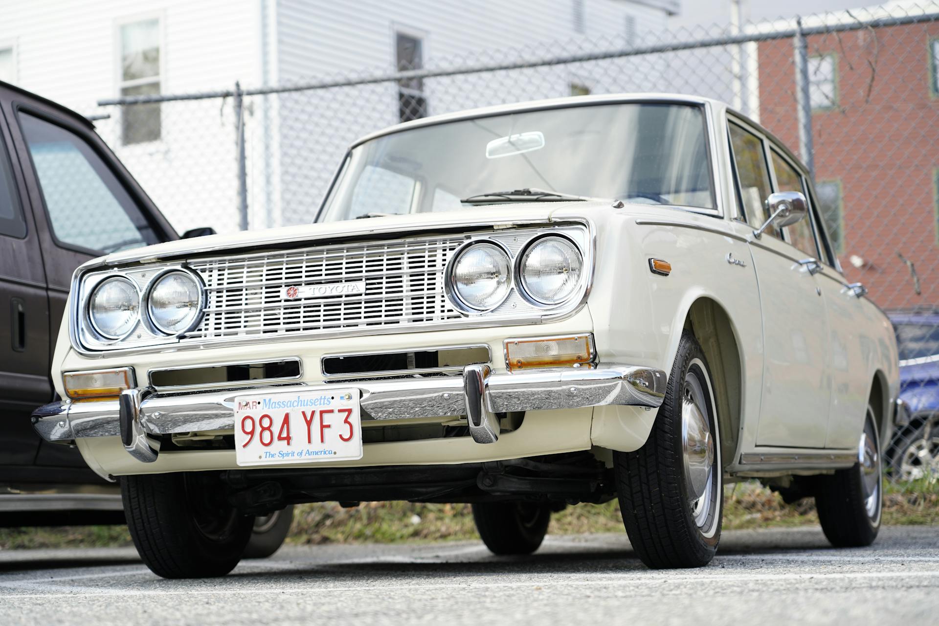 A vintage Toyota Corona car parked in an urban lot with Massachusetts plate.