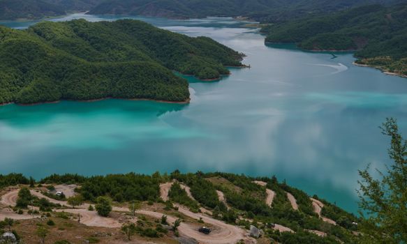 A breathtaking aerial view of a turquoise lake enveloped by lush green hills, showcasing the beauty of nature.