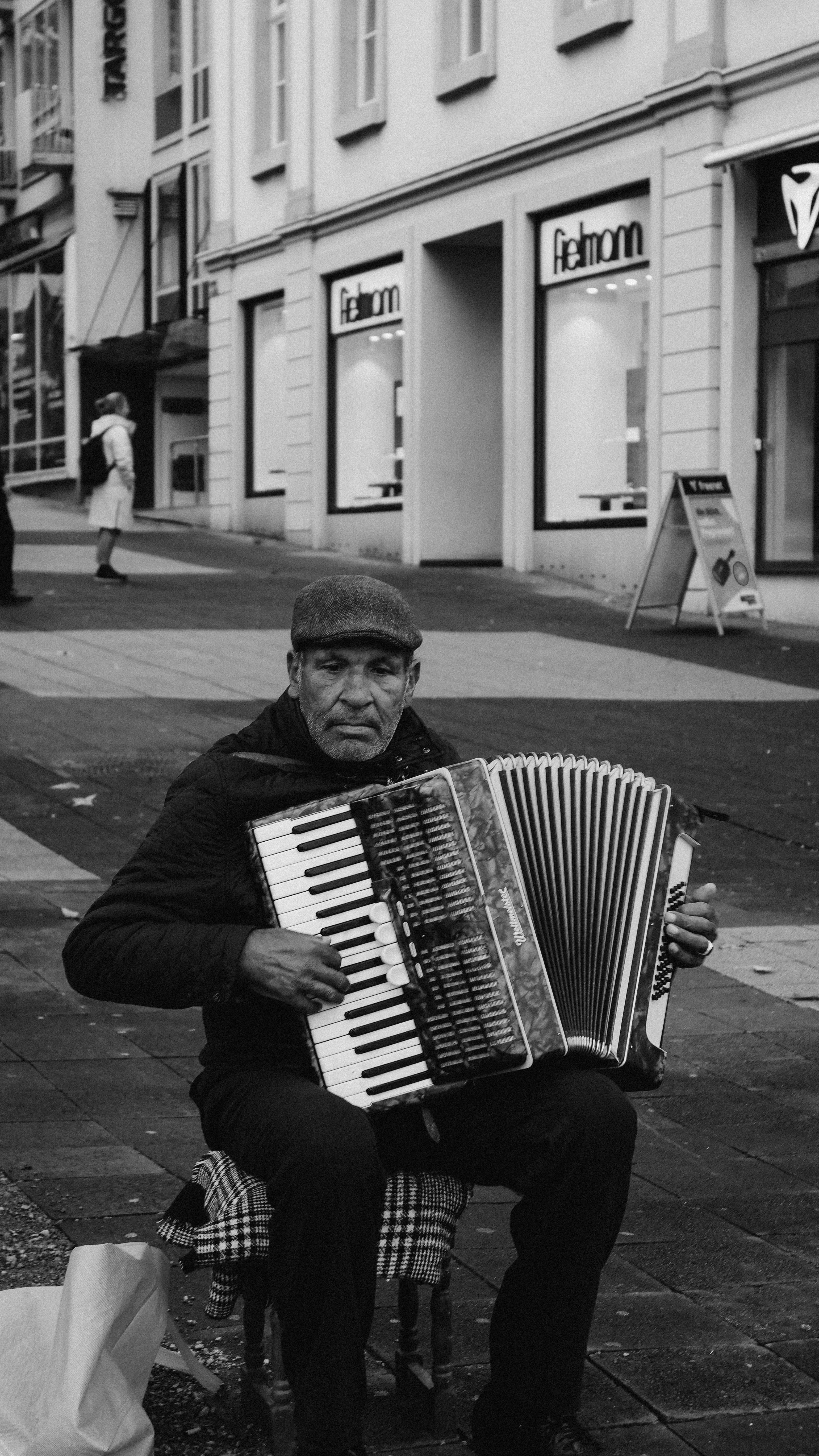 Black and white photo of a street musician playing accordion on city sidewalk.