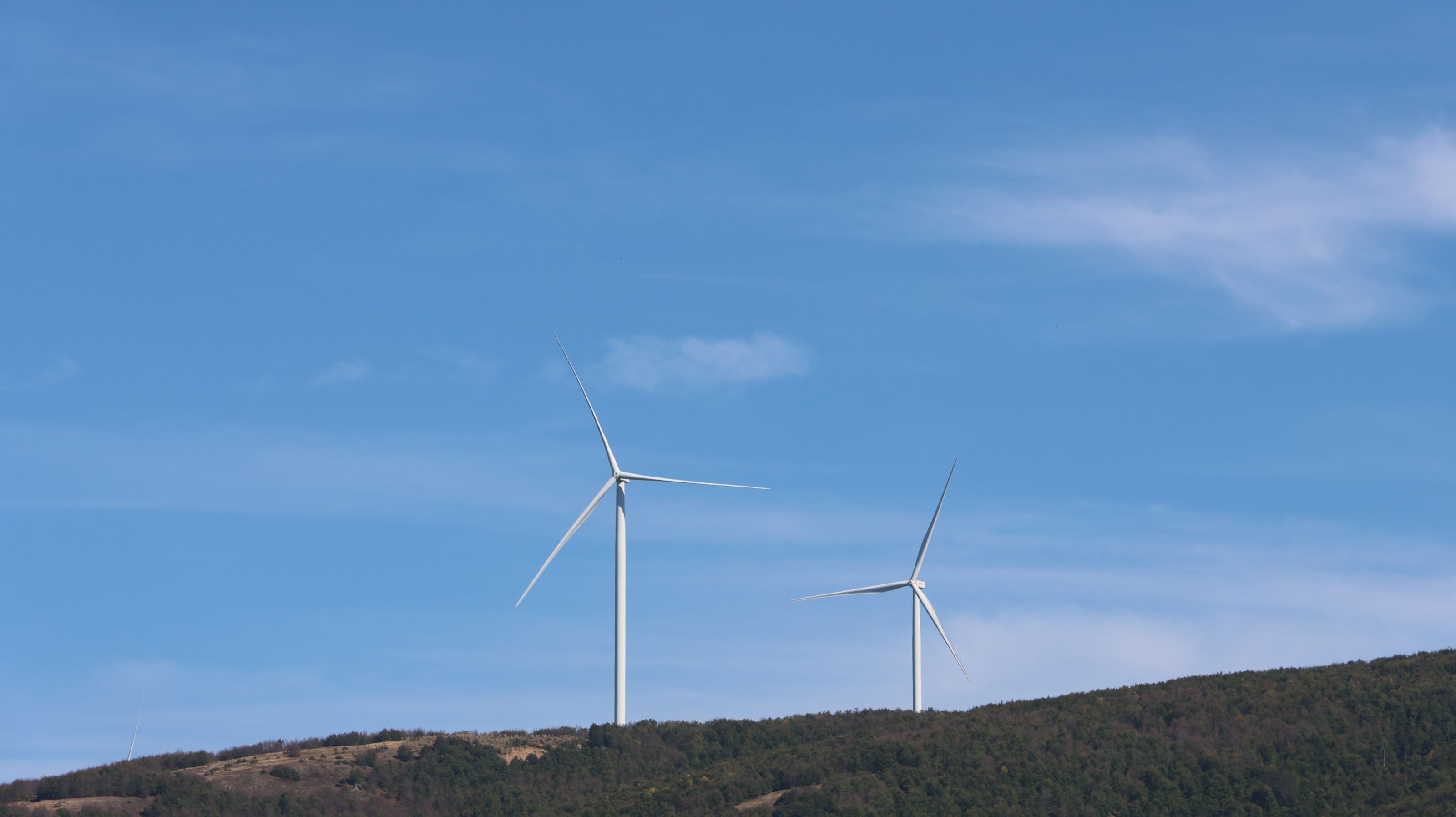 Wind turbines stand tall on Bajgora hill, generating clean energy against a clear blue sky.