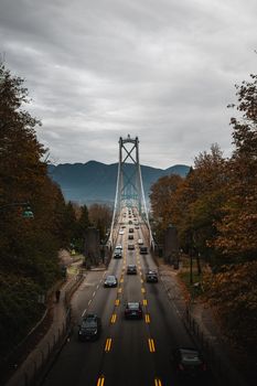 Autumn view of Lions Gate Bridge in Vancouver with traffic and cloudy sky.