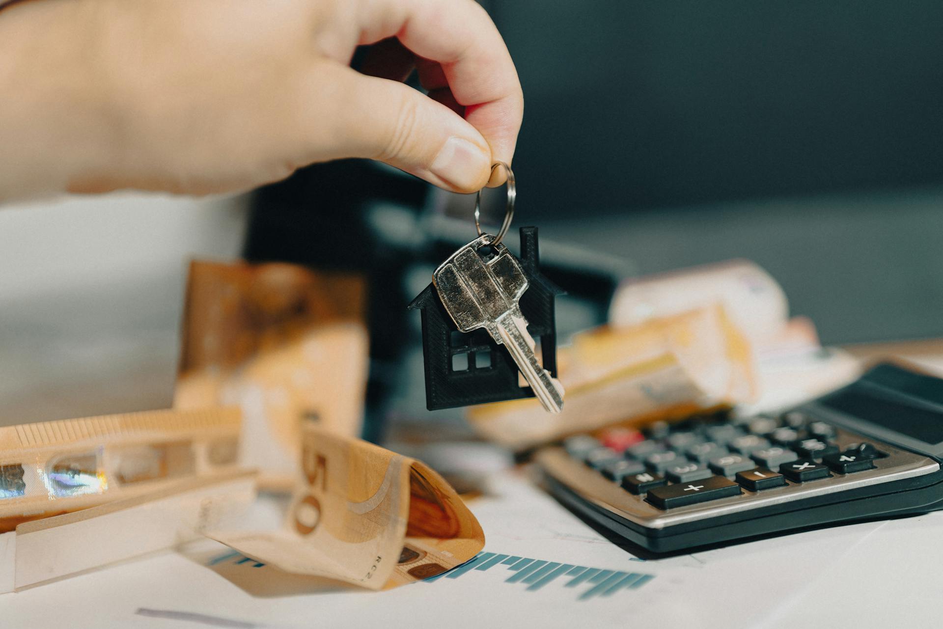 Close-up of a hand holding keys over euros and calculator, symbolizing real estate purchase.