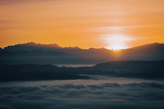 A stunning sunrise over a mountainous landscape with clouds, creating a dramatic and serene scene.