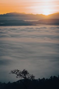 Capture the serene beauty of a sunrise above a vast blanket of clouds with distant mountains.