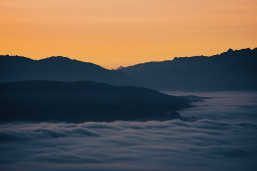 Free A peaceful mountain landscape with fog under a vibrant sunrise sky. Ideal for calm and nature-focused themes. Stock Photo