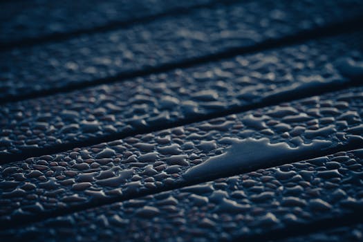 Macro view of raindrops on a wooden surface, highlighted with cool blue lighting, creating a calming texture.