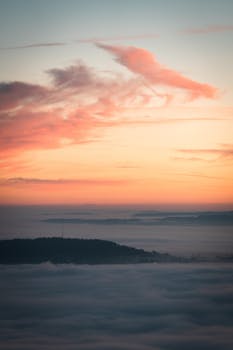 A stunning view of a sunrise with pink clouds over misty mountains, showcasing nature's serene beauty.