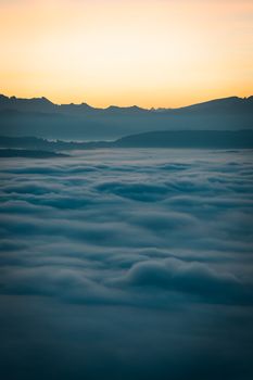 Peaceful mountain scenery with clouds below and a warm sunrise illuminating the horizon.