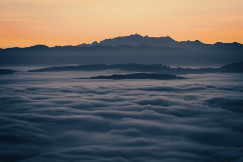 Free Panoramic view of mountains silhouetted against a sunrise sky above a sea of clouds. Stock Photo