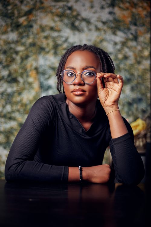 Free A confident woman poses in a studio, wearing blue glasses and a black top, against a textured green background. Stock Photo