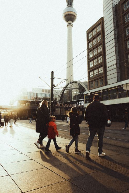 Free A family strolls through Berlin's Alexanderplatz with the iconic TV Tower in view during golden hour. Stock Photo