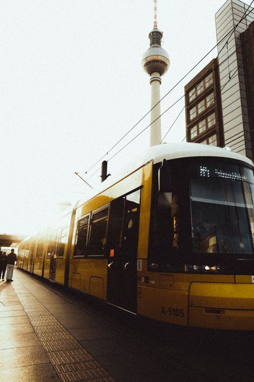 Free Berlin Alexanderplatz with a vibrant yellow tram and the iconic TV tower perfect for cityscape photography. Stock Photo