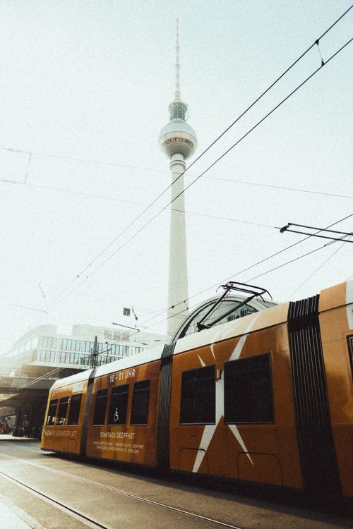 Free Capture of a yellow tram passing under the iconic Berlin TV Tower during the day in Alexanderplatz. Stock Photo