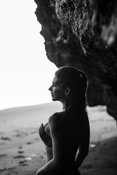 Black and white silhouette of a woman standing in a beach cave, creating a dramatic contrast.