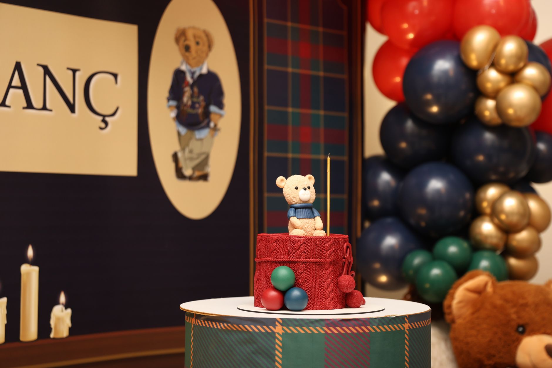 first birthday party planning egypt — Teddy bear cake topper with vibrant balloons and plaid backdrop at a festive celebratio
