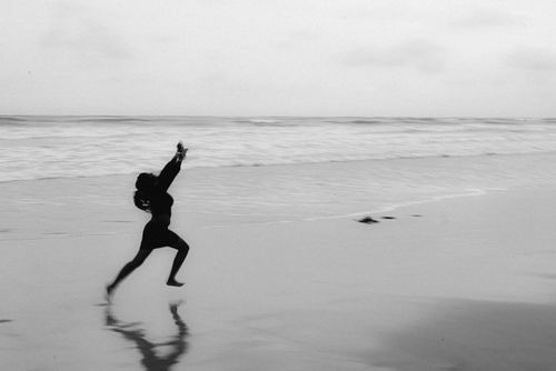 Free Black and white photo of a person running on a serene beach, reflecting freedom. Stock Photo