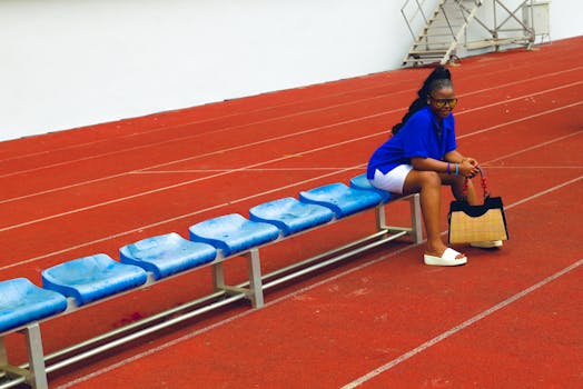 Woman sitting on blue bench in sports track area holding a fashionable handbag.