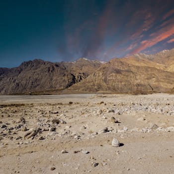 Breathtaking view of Nubra Valley's rugged terrain under a colorful sunset sky in Ladakh, India.