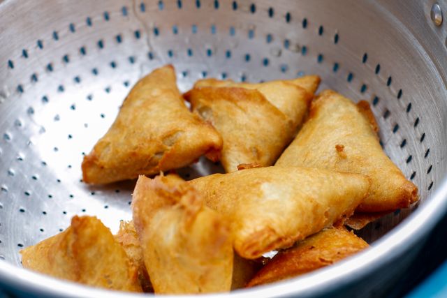 Crispy golden fried samosas placed in a stainless colander, perfect for a savory snack.