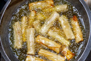 Pale spring rolls bubbling in hot oil inside a dark round frying pan