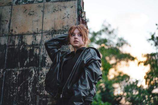Stylish young woman in leather jacket posing outdoors against an urban backdrop.