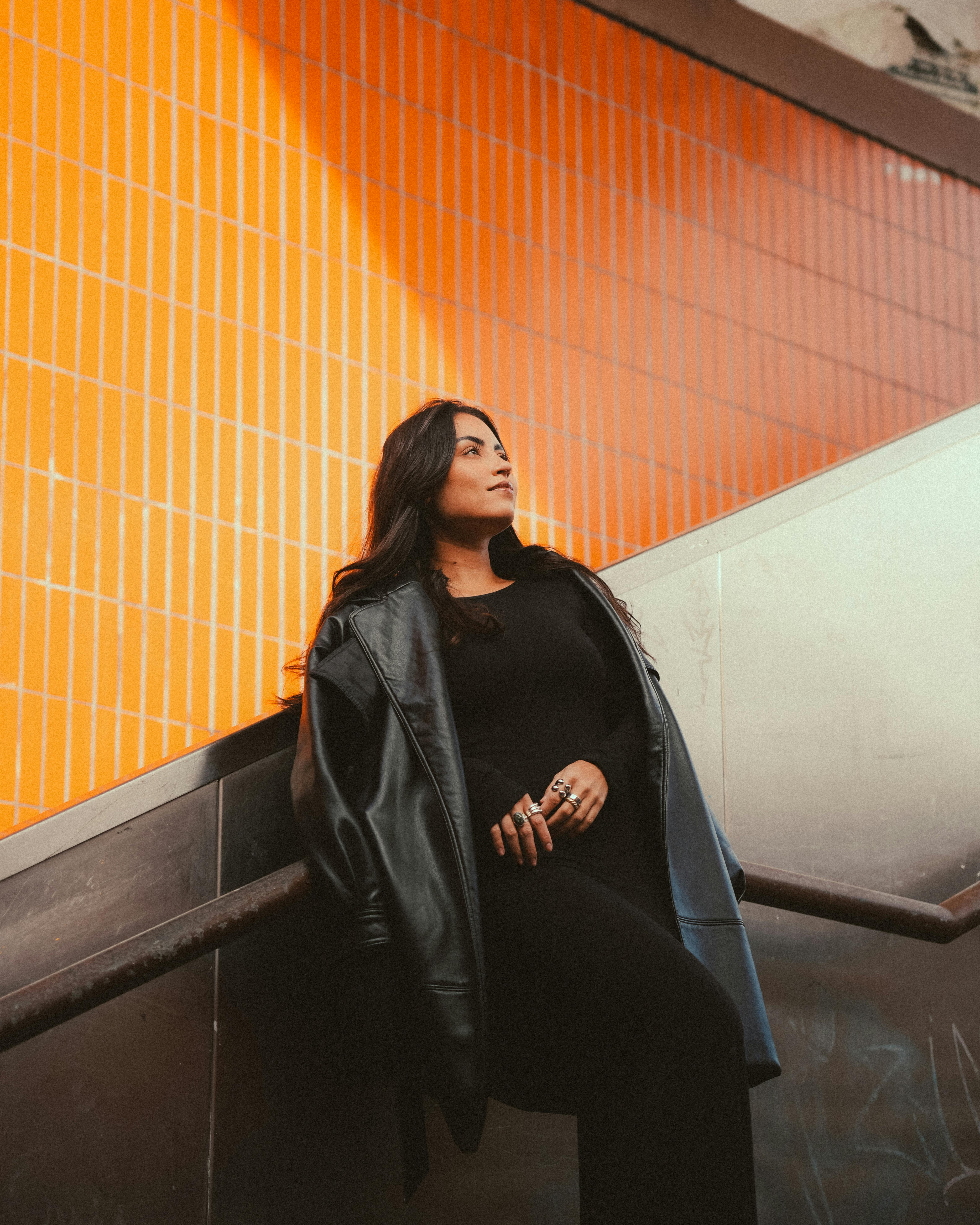 Confident woman leaning on stair railing in urban setting with vibrant orange tiles.