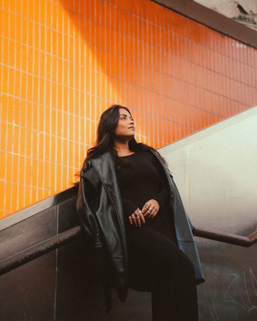 Free Confident woman leaning on stair railing in urban setting with vibrant orange tiles. Stock Photo