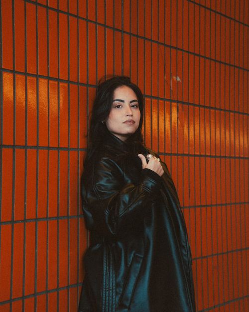 Free Confident woman poses against an orange tiled wall wearing a black leather jacket. Stock Photo