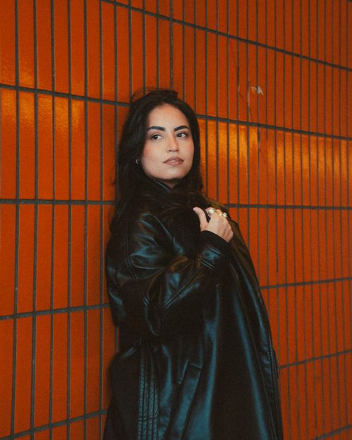 Free Trendy woman in black leather coat against a vibrant orange tiled wall. Stock Photo
