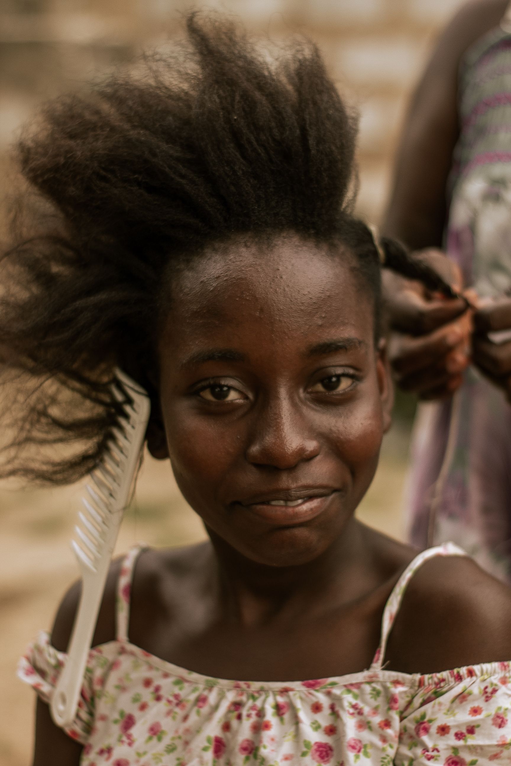 Smiling young girl having her hair styled outdoors by another person.