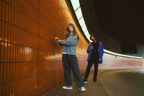Free Stylish duo poses in a dimly lit urban tunnel with orange tiled walls. Stock Photo