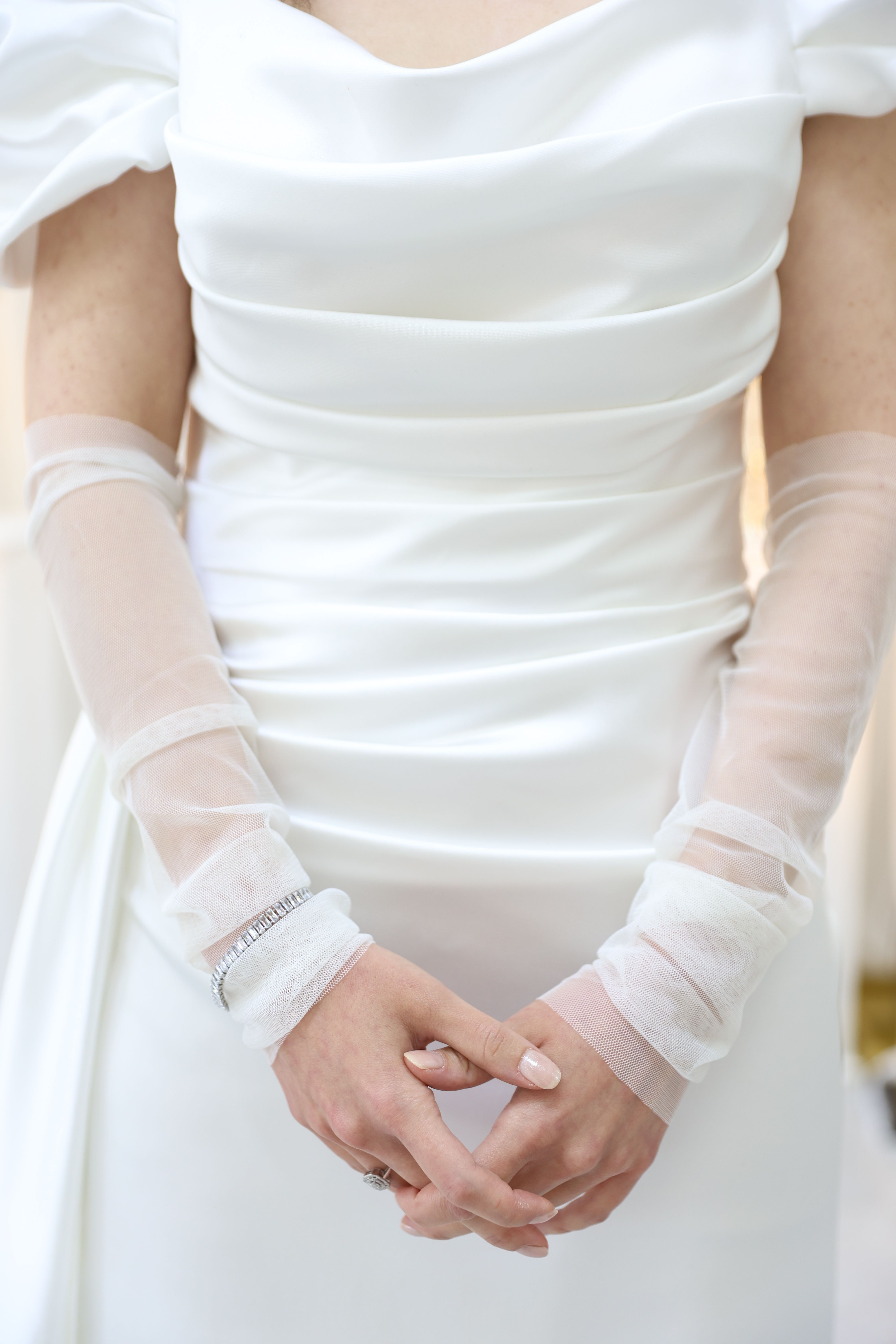 A close-up of a bride in a white wedding dress with delicate sheer sleeves.