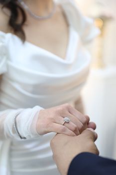 Close-up of a bride in white gown and groom holding hands, symbolizing love.