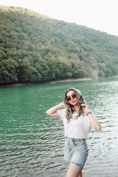 Stylish woman with sunglasses posing by a turquoise river surrounded by lush greenery in Amasya, Türkiye.