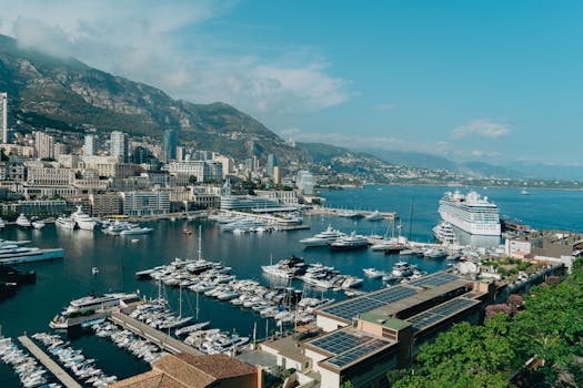 View of Monaco marina with luxury yachts and cityscape against mountainous backdrop.
