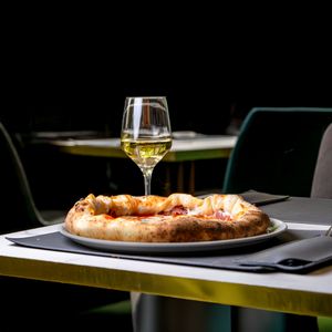 Pizza and a glass of white wine on a restaurant table — photo by Nano Erdozain on Pexels