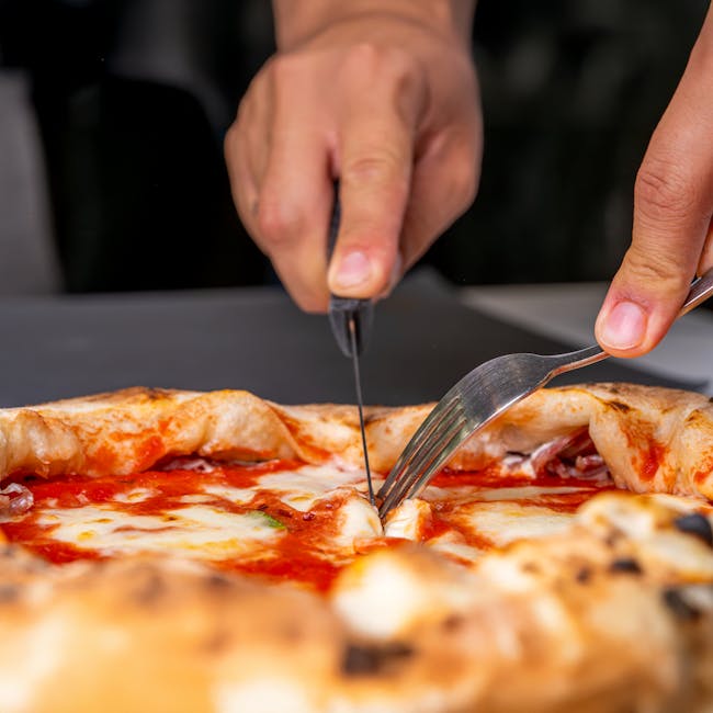 Hands cutting a cheesy pizza slice with fork and knife, capturing the savory delight.