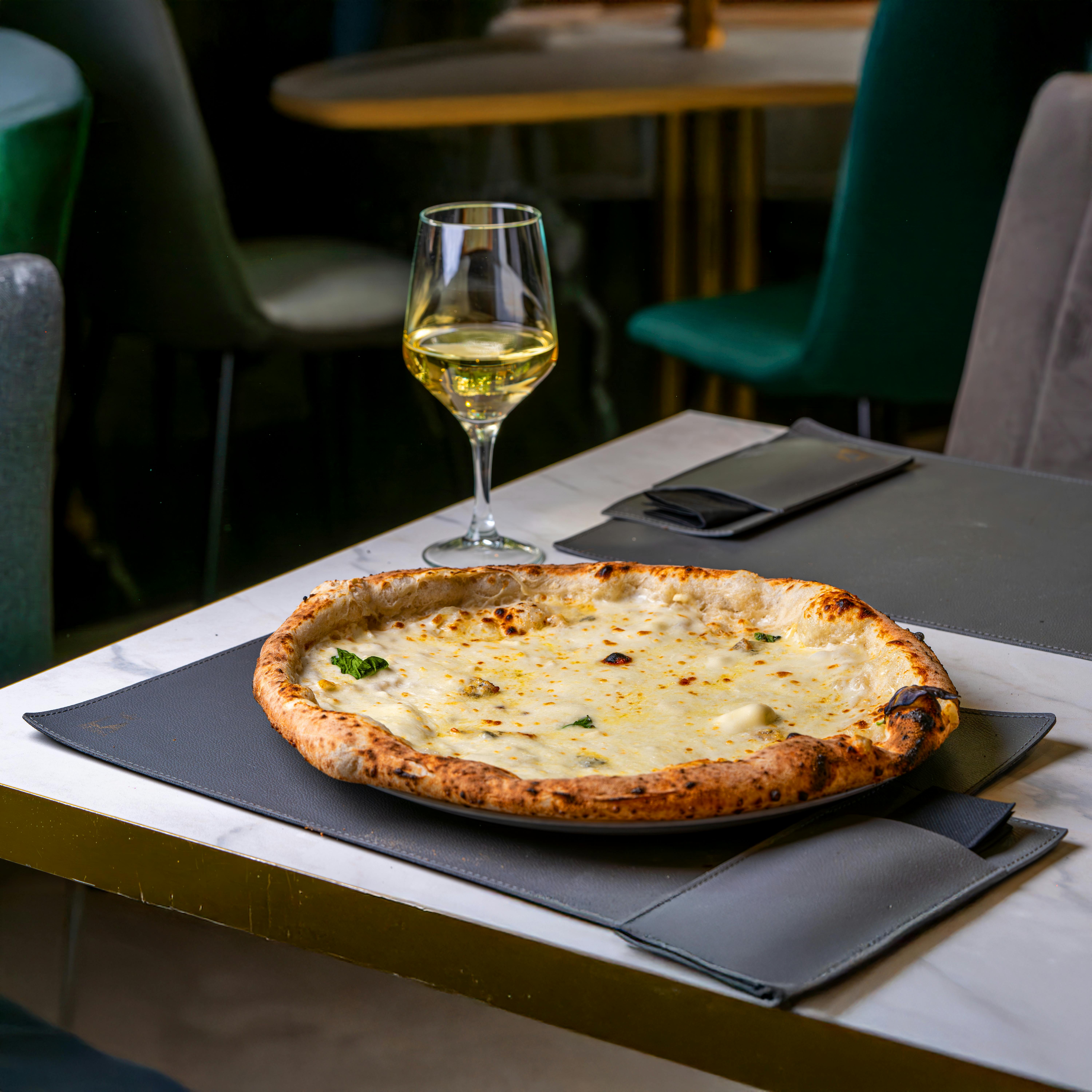 A delectable Italian pizza served with white wine on a modern indoor table setting.