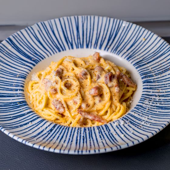 Spaghetti in glossy golden egg sauce with guanciale pieces and black pepper in a striped bowl