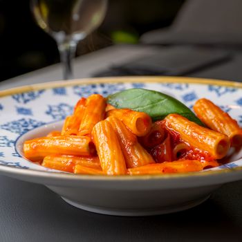 Close-up of tasty rigatoni pasta in rich tomato sauce garnished with fresh basil.