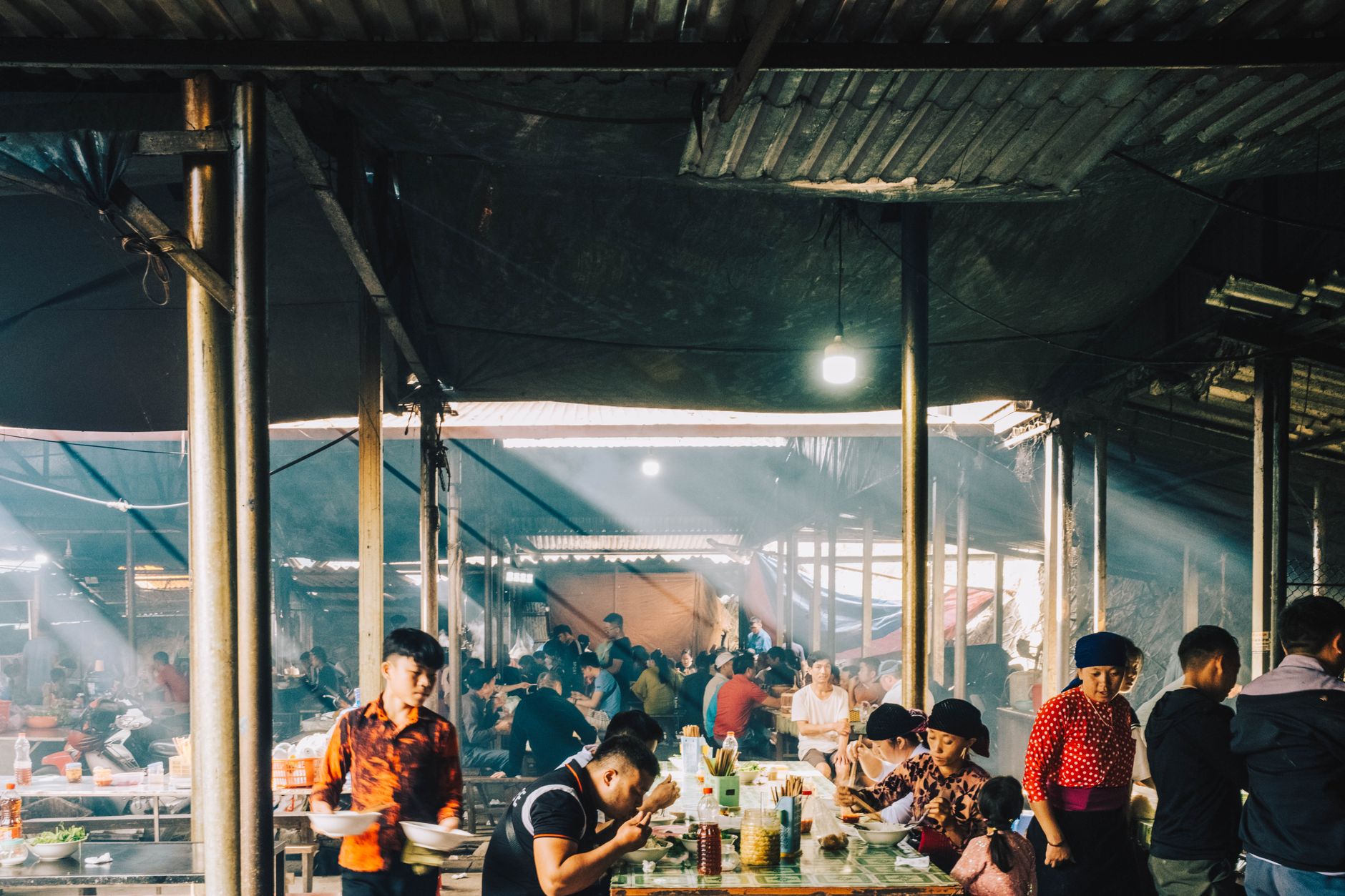 Vibrant scene of people dining and socializing inside a lively Asian market setting.