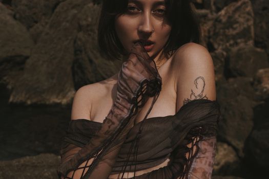 A captivating portrait of a woman with unique tattoo art, set against a rocky outdoor background.